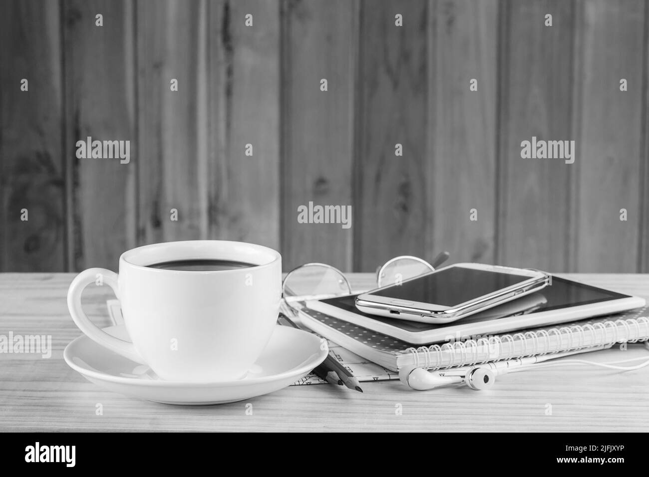 Nota libro, smartphone, tazza da caffè e pila di libri su sfondo tavolo in legno.tonalità bianco e nero Foto Stock