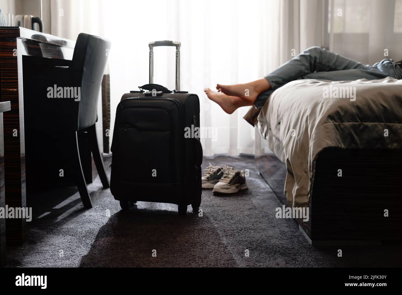 donna che prende le scarpe in una camera d'albergo sul letto. Relax in camera dopo aver viaggiato con la valigia. Femmina che si riposa dopo molto tempo Foto Stock