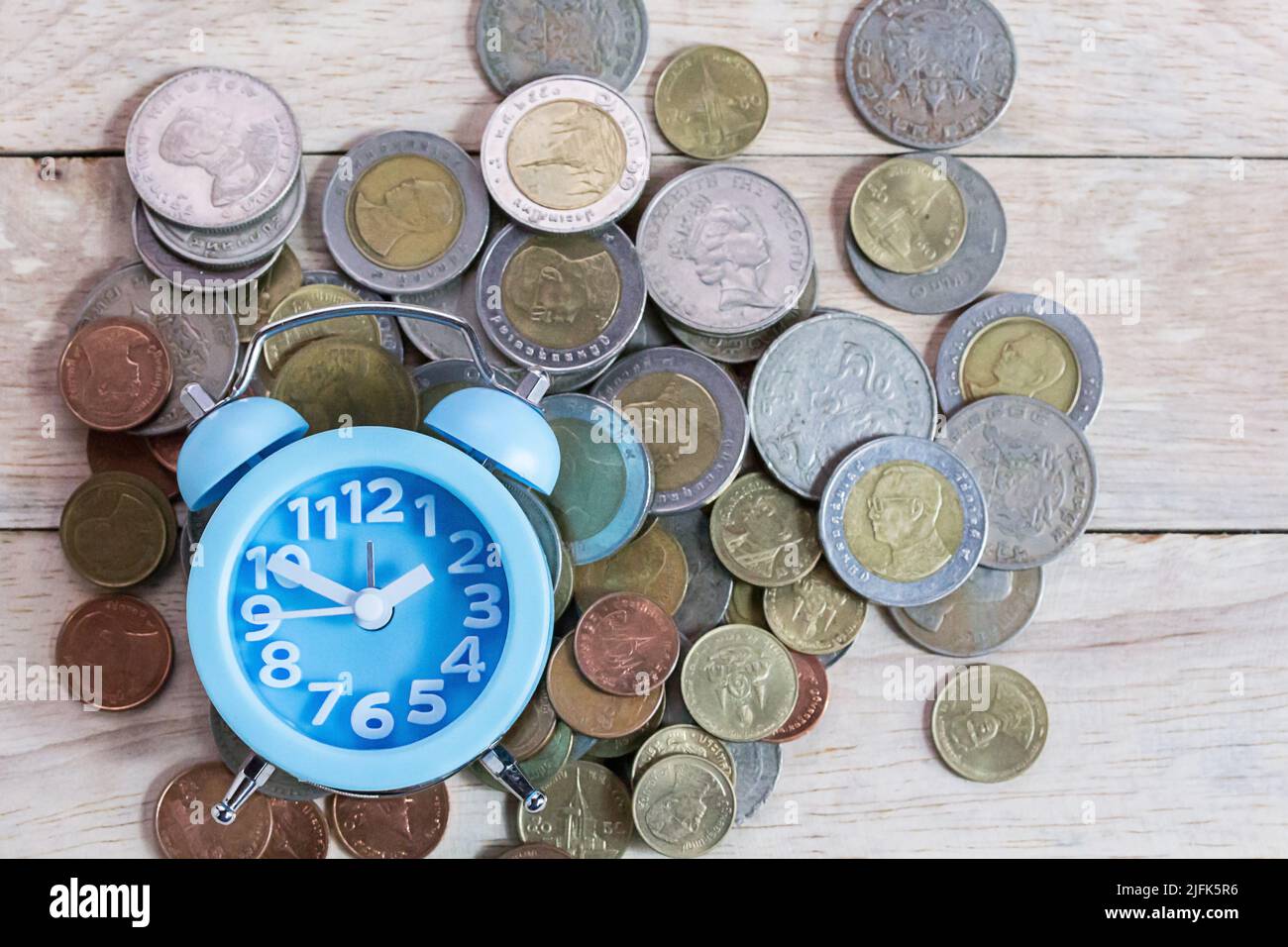 Monete, orologio alram e matita con notebook vuoto su sfondo tavola di legno. Scrivania da ufficio con monete e concetto di pianificazione finanziaria aziendale Foto Stock