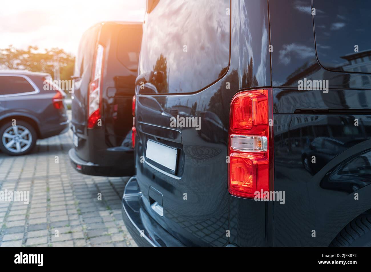 Primo piano dettaglio luce di coda vista di molti moderni furgoni neri di lusso parcheggiati in fila presso la vendita auto noleggio concessionario di leasing contro il tramonto. Trasferimento commerciale Foto Stock