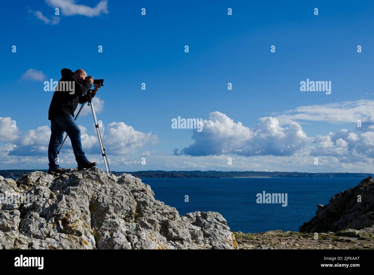 Fotografo all'aperto in piedi su una roccia e scattare foto del paesaggio mozzafiato della Bretagna vicino Pointe de Penhir. Foto Stock