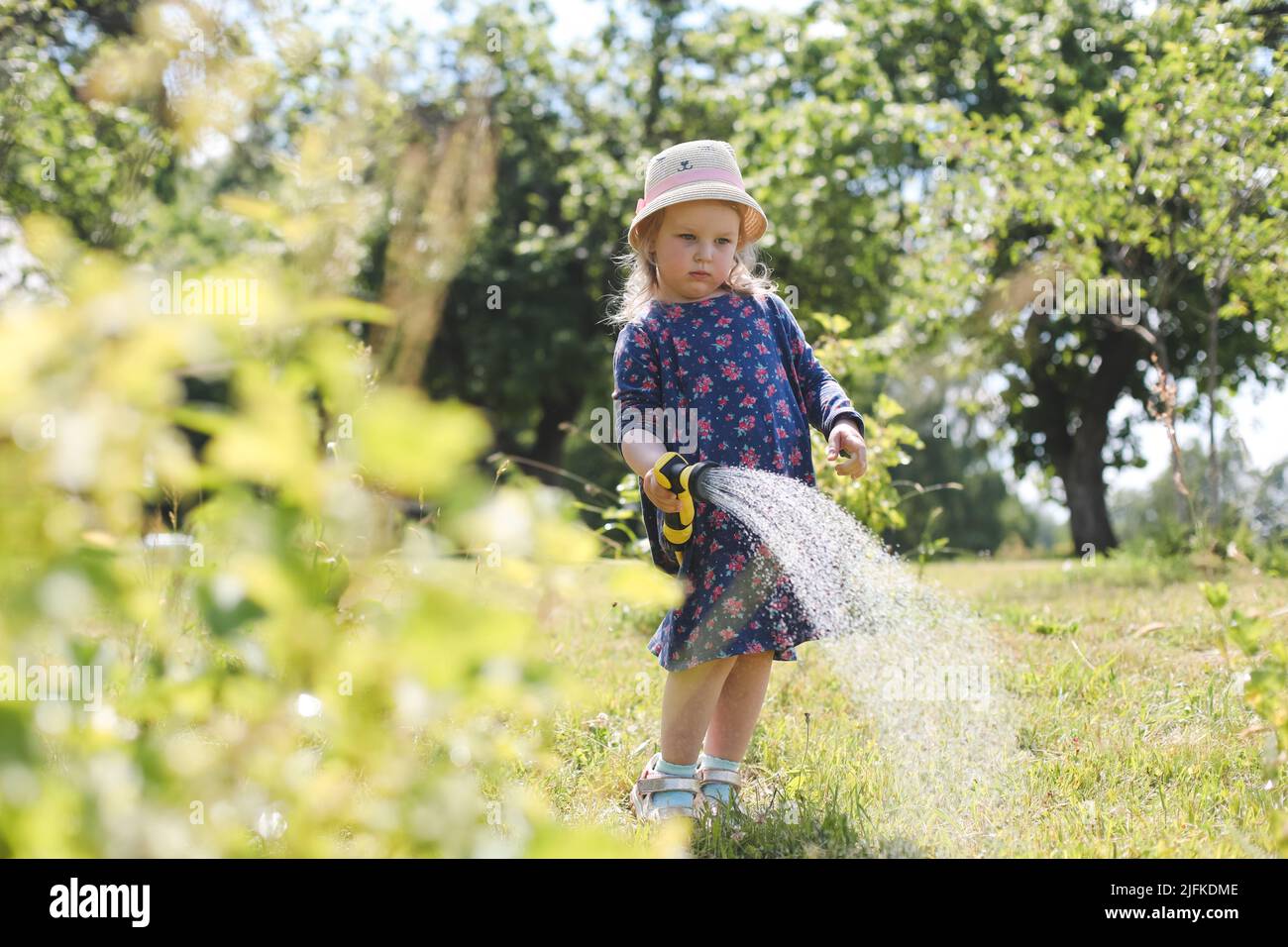 Adorabile bambina che gioca con una manichetta da giardino nella giornata estiva calda e soleggiata Foto Stock