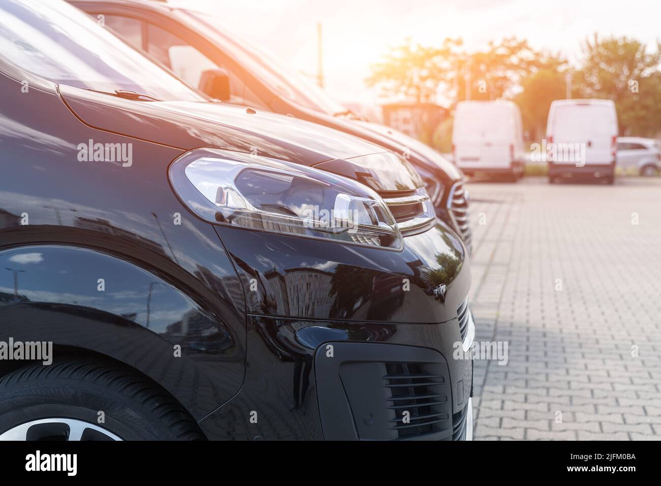 Primo piano dettaglio vista faro di molti moderni furgoni neri di lusso parcheggiati in fila alla vendita auto noleggio concessionario di leasing contro tramonto. Trasferimento commerciale Foto Stock