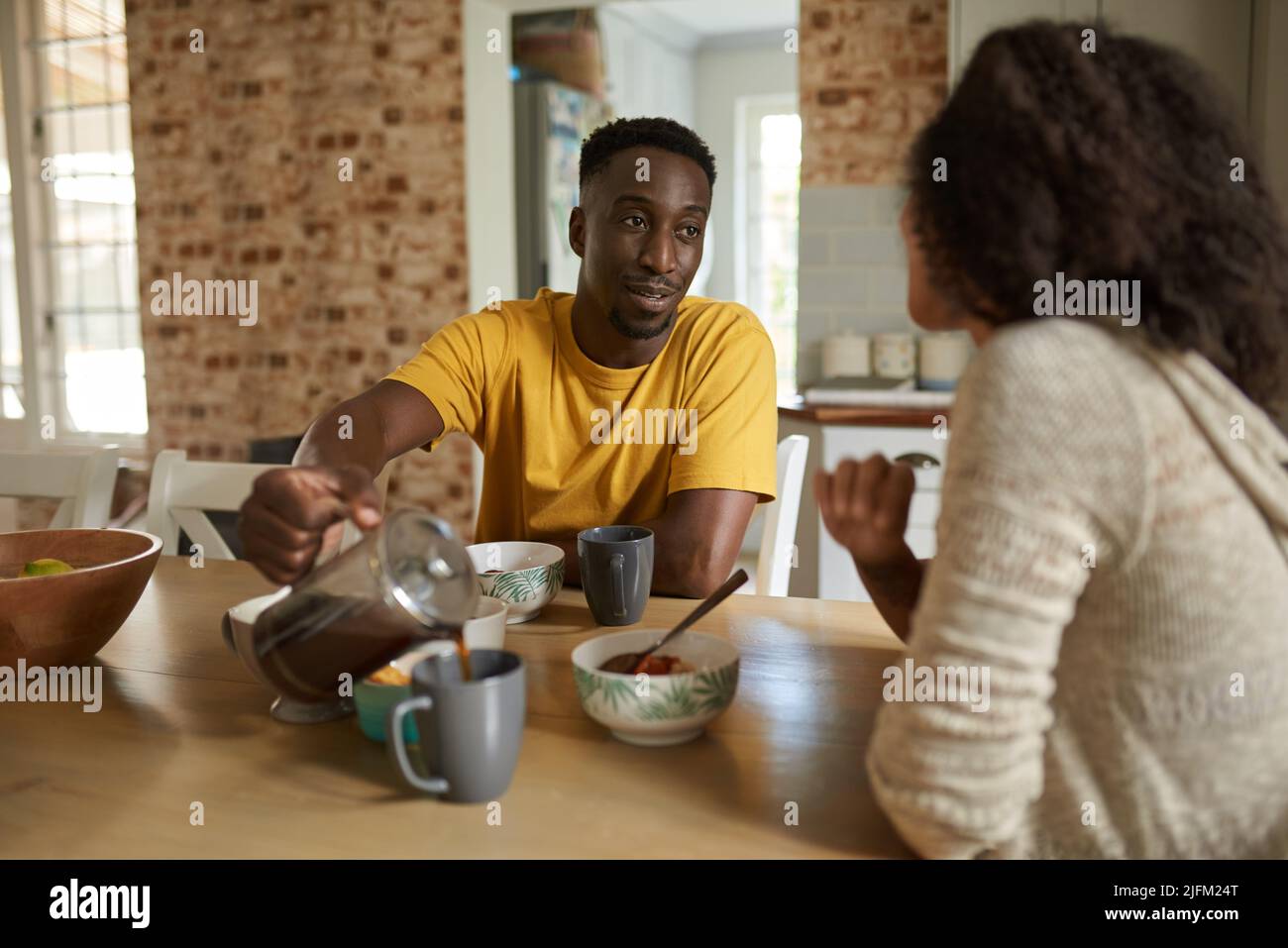 Il giovane uomo africano che versa il caffè per sua moglie durante la colazione Foto Stock
