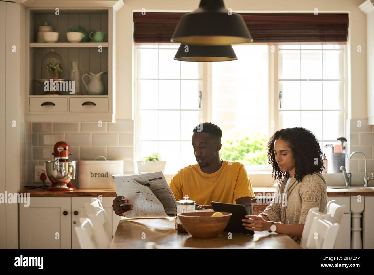Giovani coppie multietniche che si ritrovano a prendere notizie durante la colazione in cucina Foto Stock