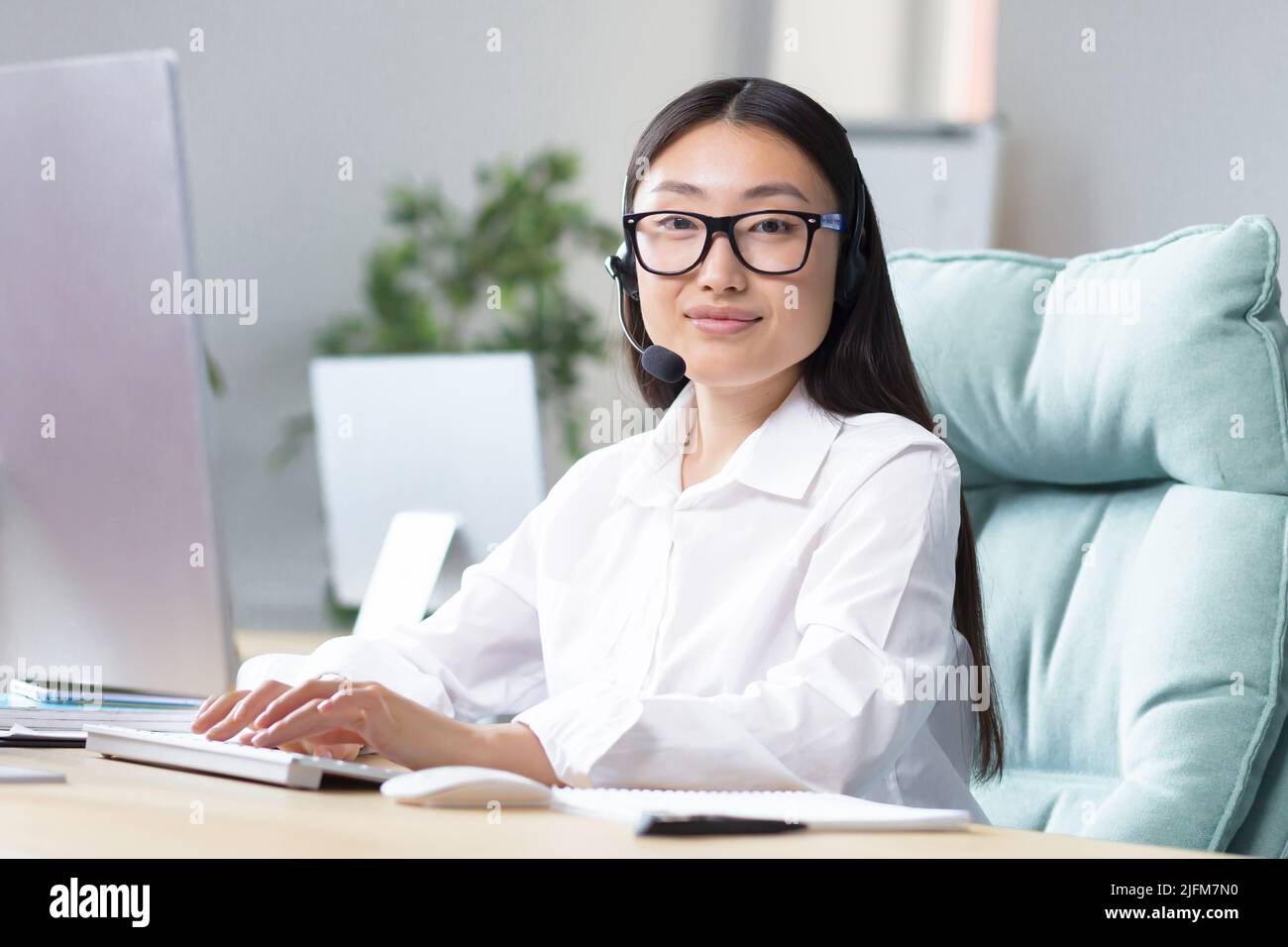 Giovane tecnico addetto al supporto, ritratto asiatico donna d'affari che lavora in un ufficio moderno al lavoro, guardando la fotocamera, utilizzando cuffie per la comunicazione video. Foto Stock