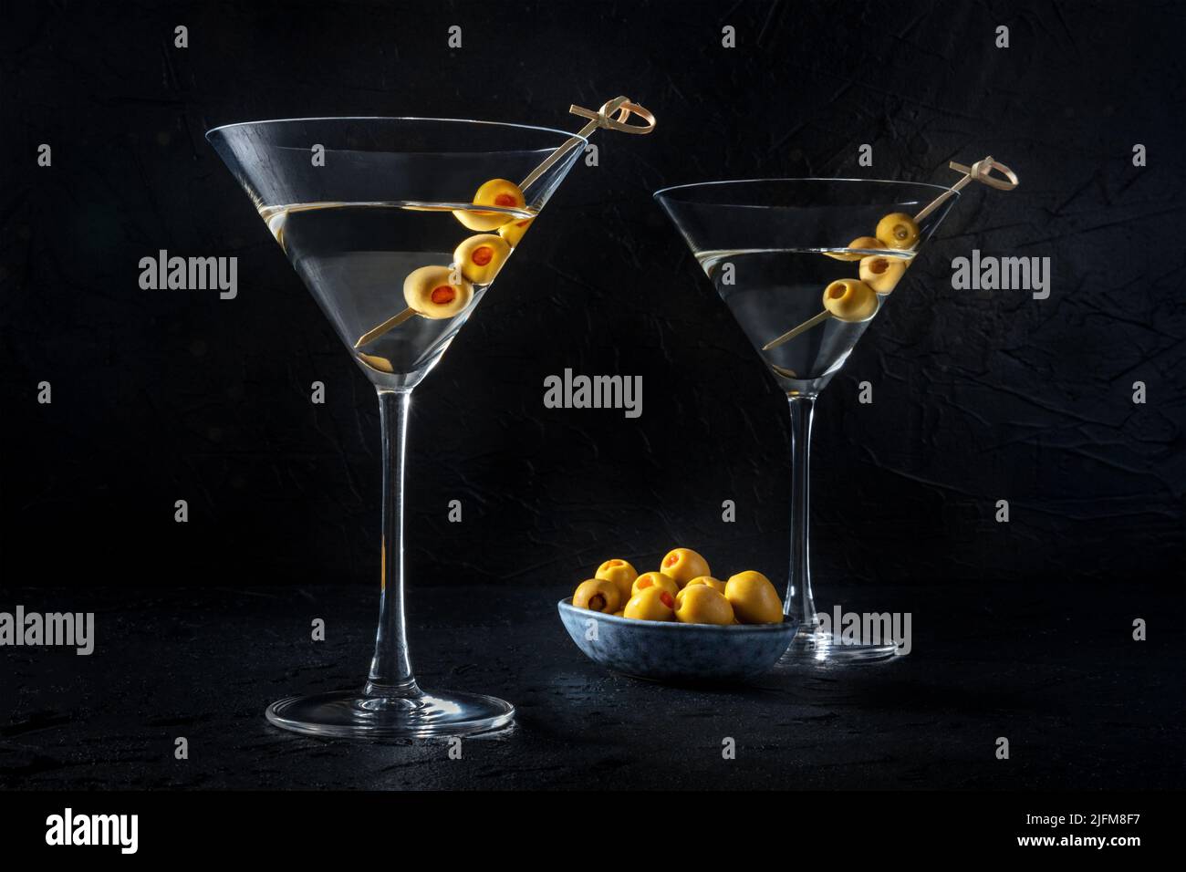 Martini, due bicchieri con olive speziate, su sfondo nero. Cocktail alcolico Foto Stock
