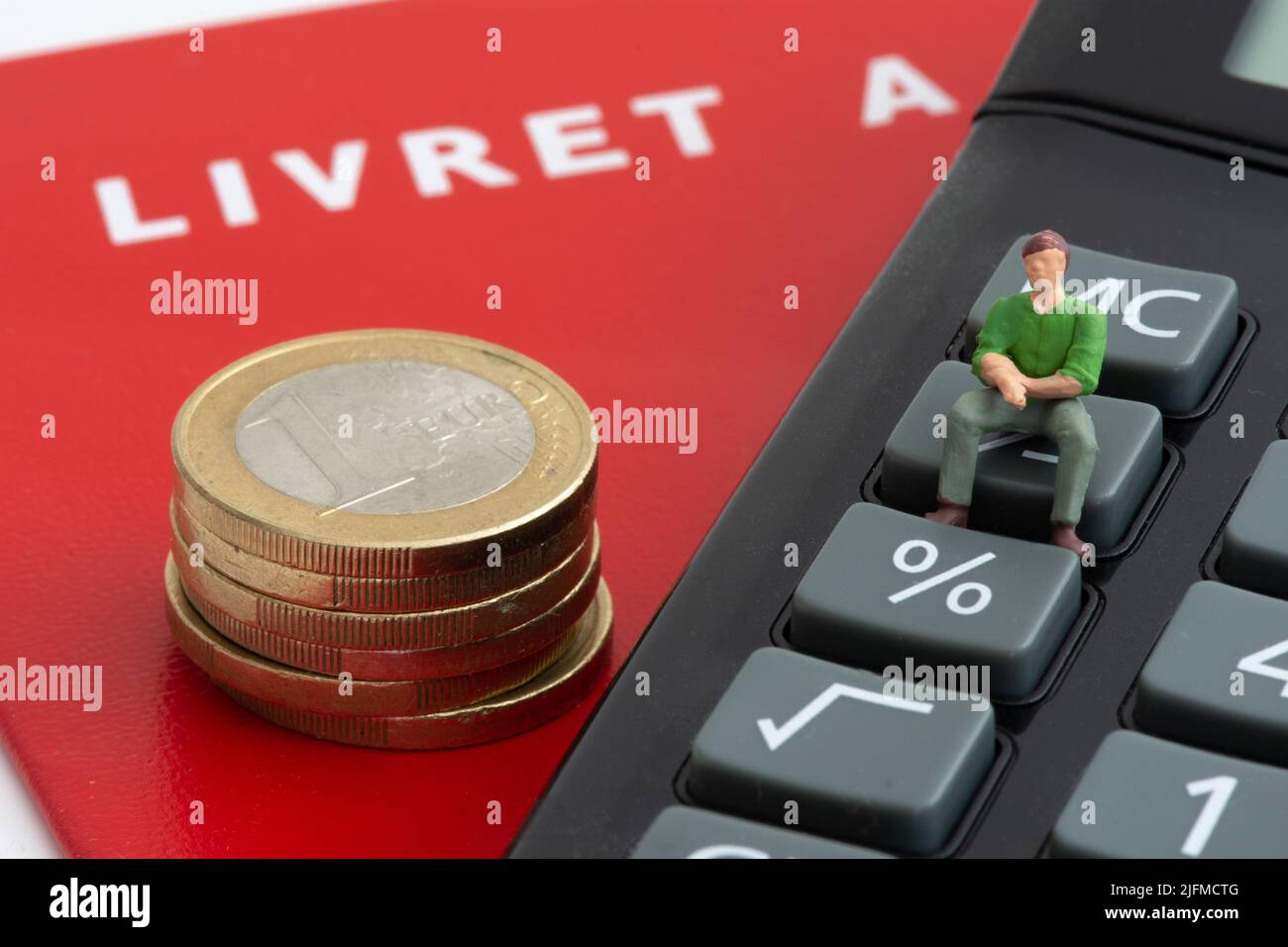 Figurine seduta su una calcolatrice vicino a una pila di monete in euro e un francese livret A. concetti di inflazione, risparmio e livret A tassi di interesse Foto Stock