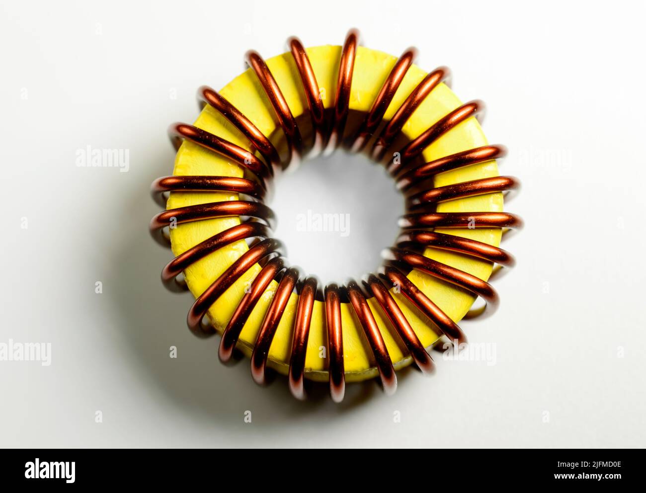 Componente induttivo, bobina filo di rame, toroide giallo - immagine macro. Isolato su sfondo bianco. Foto Stock