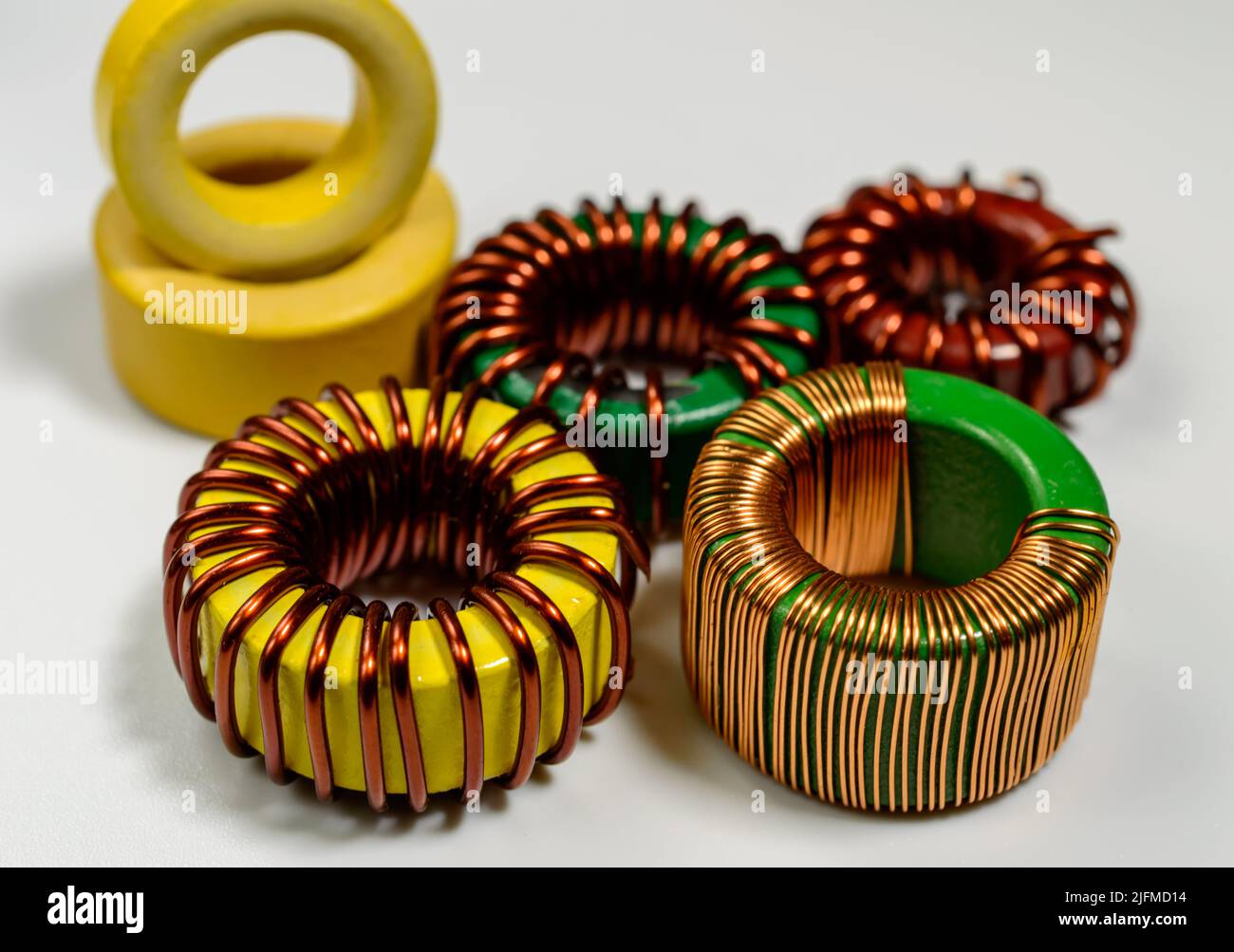 Piccola famiglia di bobine induttive su sfondo bianco. Componente induttivo, bobina filo di rame, toroide giallo - immagine macro. Foto Stock
