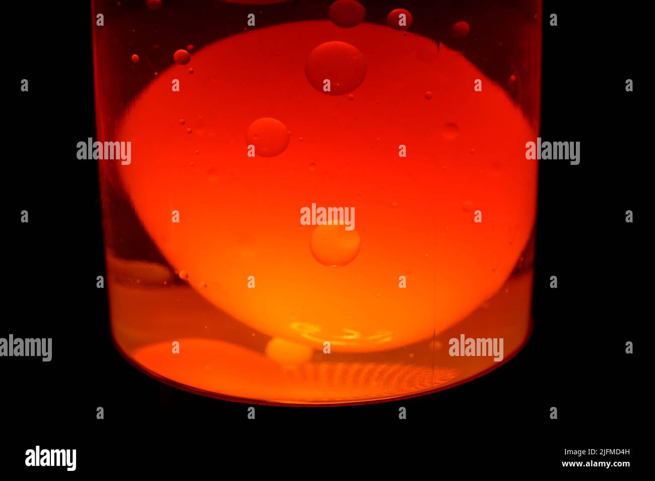 Foto macro di una lampada di lava nell'oscurità. Immagine di sfondo. Le bolle graziose stanno andando lentamente su e giù. Liquido arancione al buio. Foto Stock