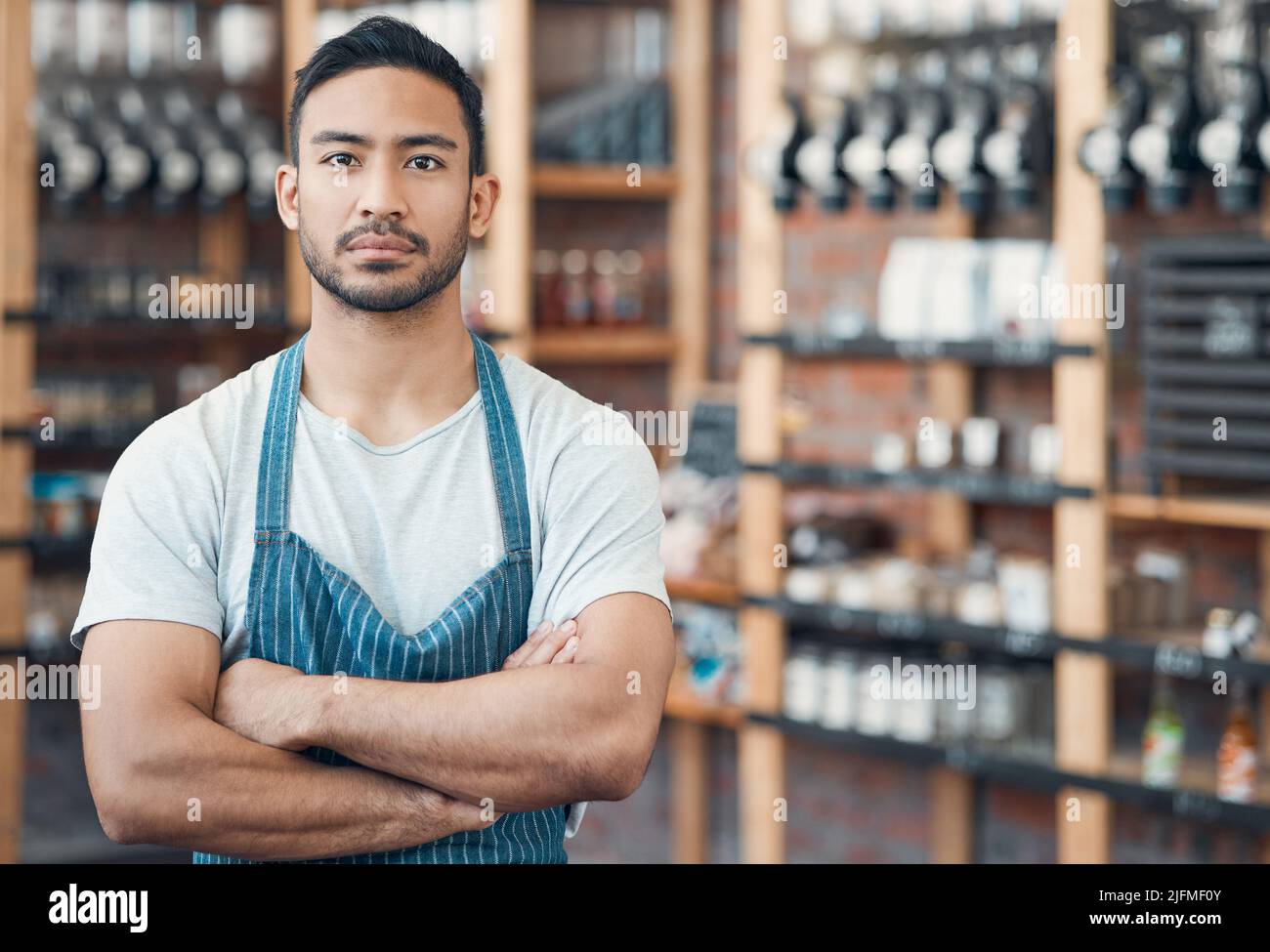 Ritratto di un giovane cameriere ispanico felice in piedi con le braccia incrociate in un negozio o caffè. Uomo concentrato e proprietario di coffee eshop che gestisce un successo Foto Stock