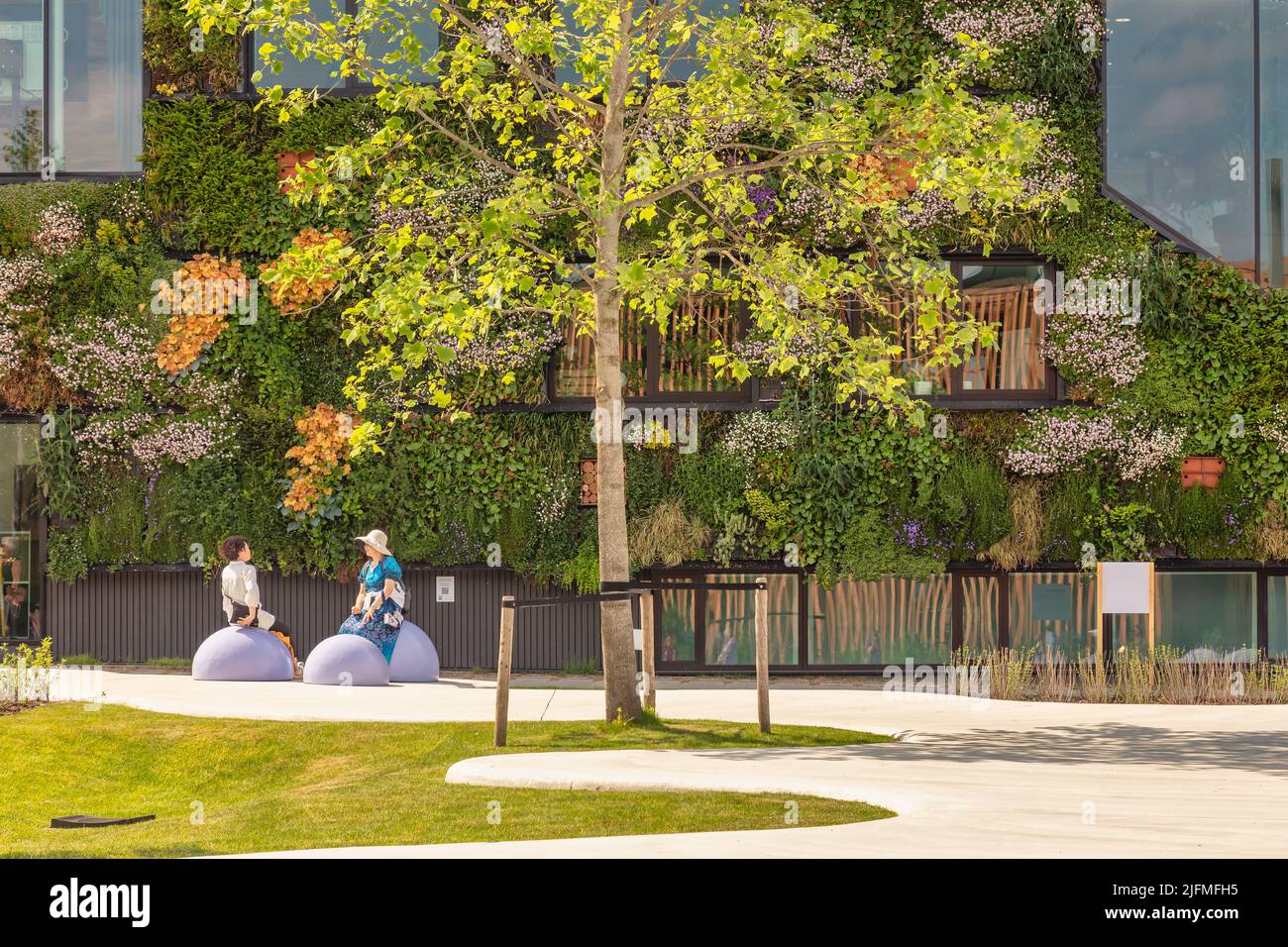 Almere, Paesi Bassi - 17 maggio 2022: Due donne che si rilassano di fronte a un edificio urbano verde di uffici sul Floriade Expo 2022 di Almere Foto Stock