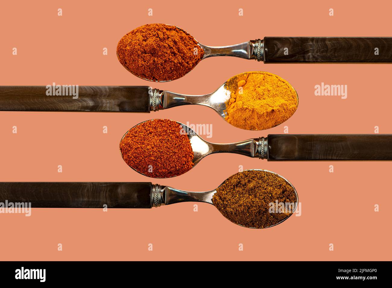 Una selezione di spezie in polvere di curry di peperoncino cayenne, utilizzate nella cucina indiana su un colorato sfondo di pesca Foto Stock