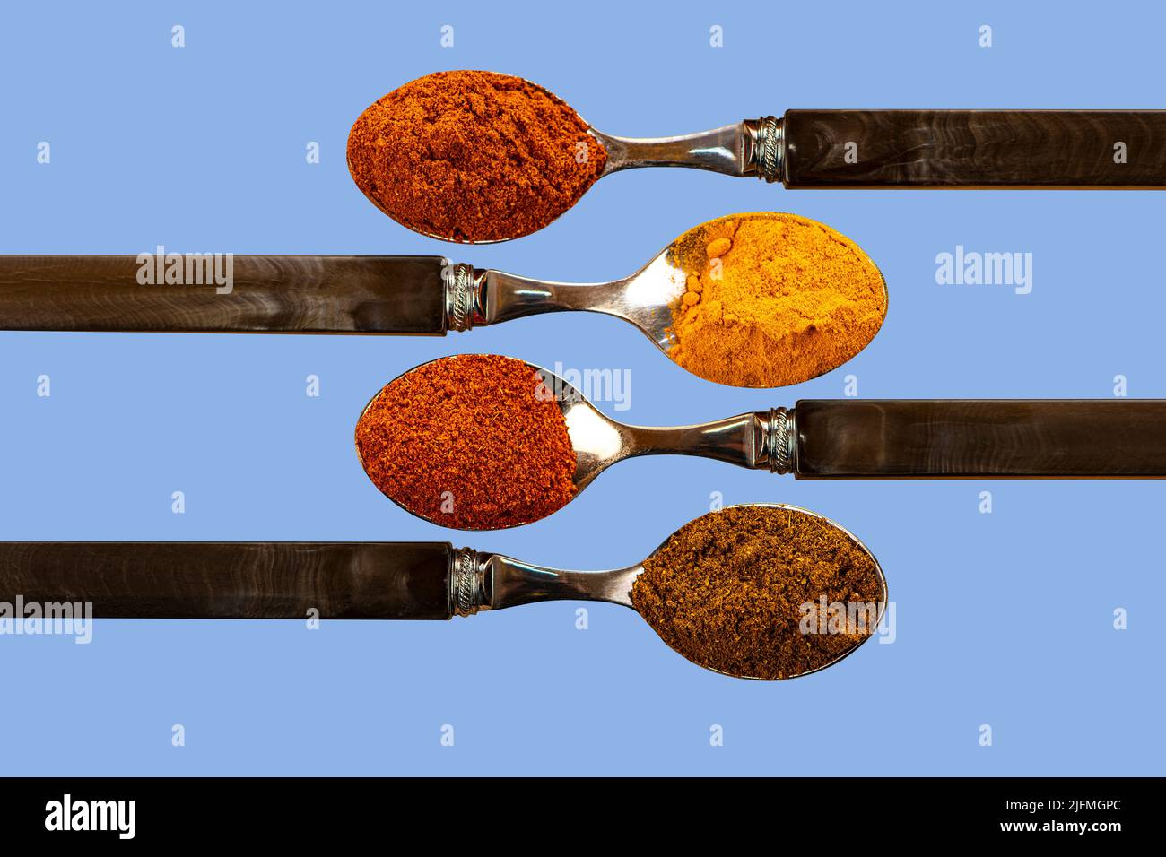 Una selezione di spezie in polvere di curry di peperoncino cayenne, utilizzate nella cucina indiana su sfondo blu colorato Foto Stock