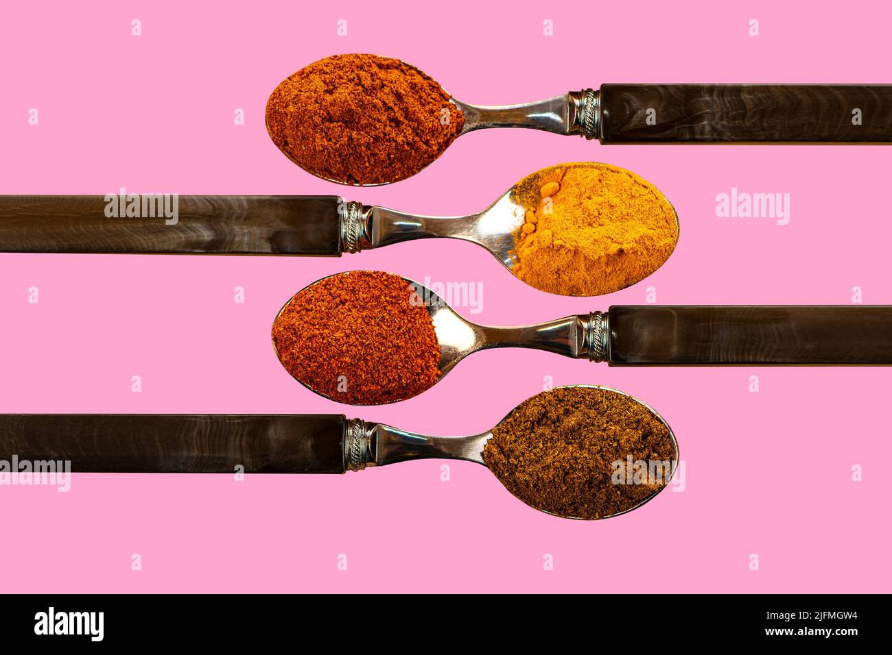 Una selezione di spezie in polvere di curry al peperoncino cayenne, utilizzate nella cucina indiana su un colorato sfondo rosa Foto Stock