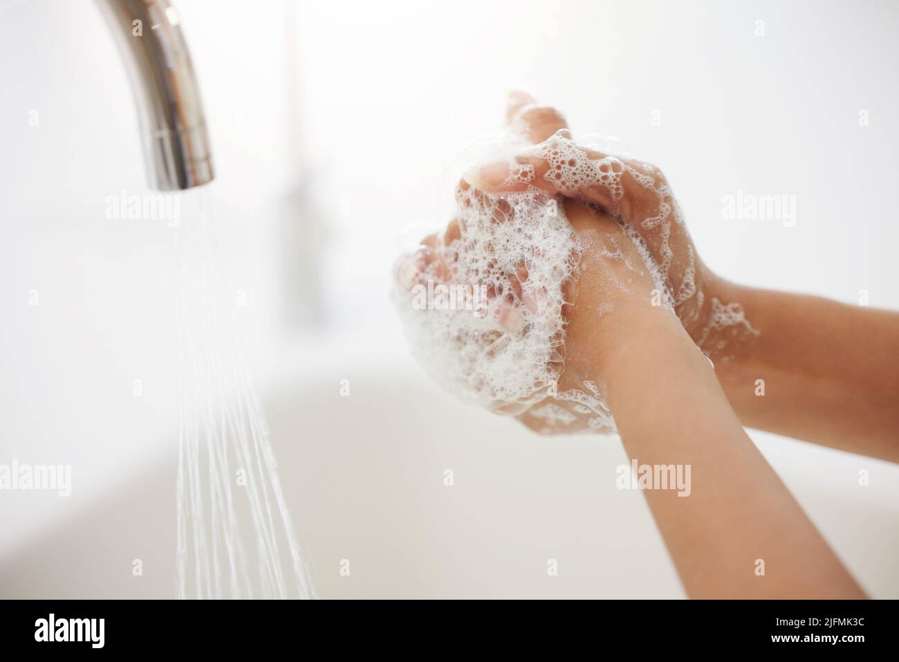 Una donna irriconoscibile lavando le mani al lavandino della cucina. Una donna sconosciuta di razza mista con le mani coperte di schiuma lavando le dita per sbarazzarsi di Foto Stock