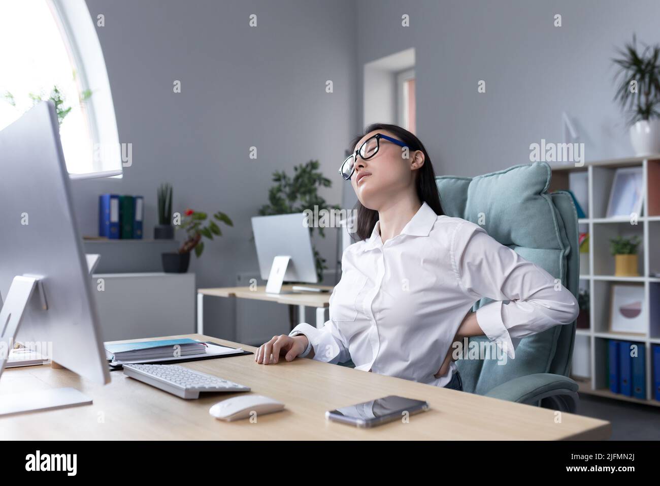 Stanco lavoratrice da ufficio femminile massaggiando la schiena, donna asiatica d'affari ha grave mal di schiena e mal di schiena più basso. Foto Stock
