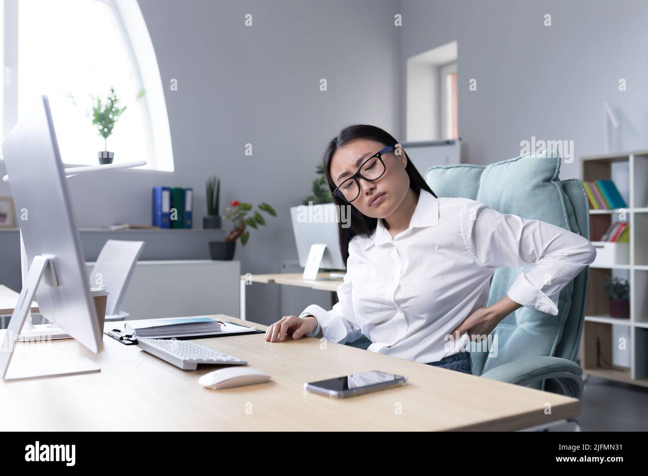 Stanco lavoratrice da ufficio femminile massaggiando la schiena, donna asiatica d'affari ha grave mal di schiena e mal di schiena più basso. Foto Stock