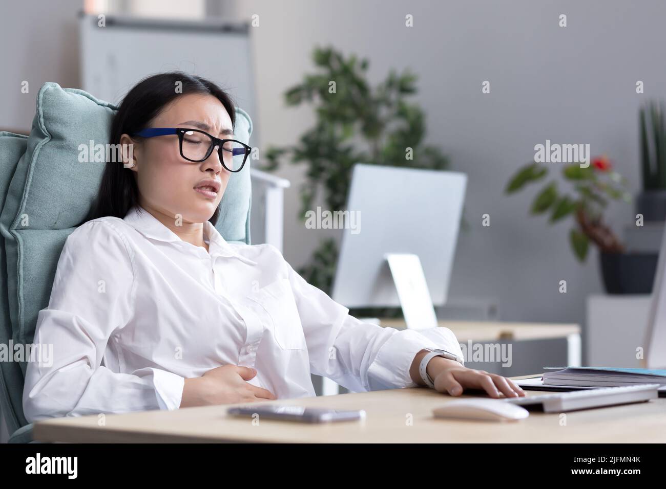La donna asiatica d'affari è ammalata nell'ufficio, ha dolore severo dello stomaco, nausea e diarrea. Foto Stock