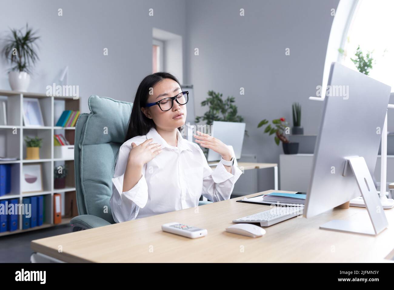 Calore in ufficio, donna asiatica che cerca di rinfrescarsi, donna d'affari che lavora al computer, agitando le mani per raffreddarsi. Foto Stock