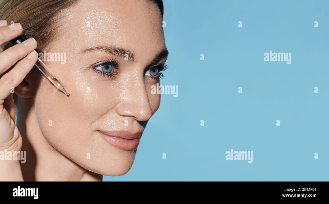 Bella donna che applica olio essenziale sul viso per una pelle idratata utilizzando un contagocce per pipette. cura della pelle del viso con olio e siero essenziali per il trattamento Foto Stock