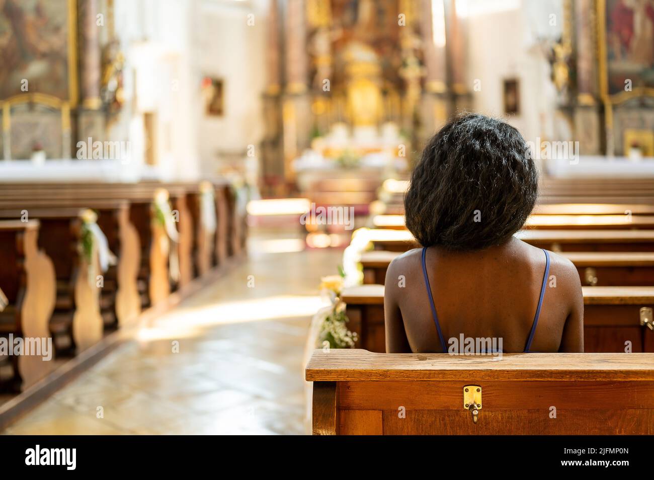 Una donna siede sola e sola in una chiesa Foto Stock