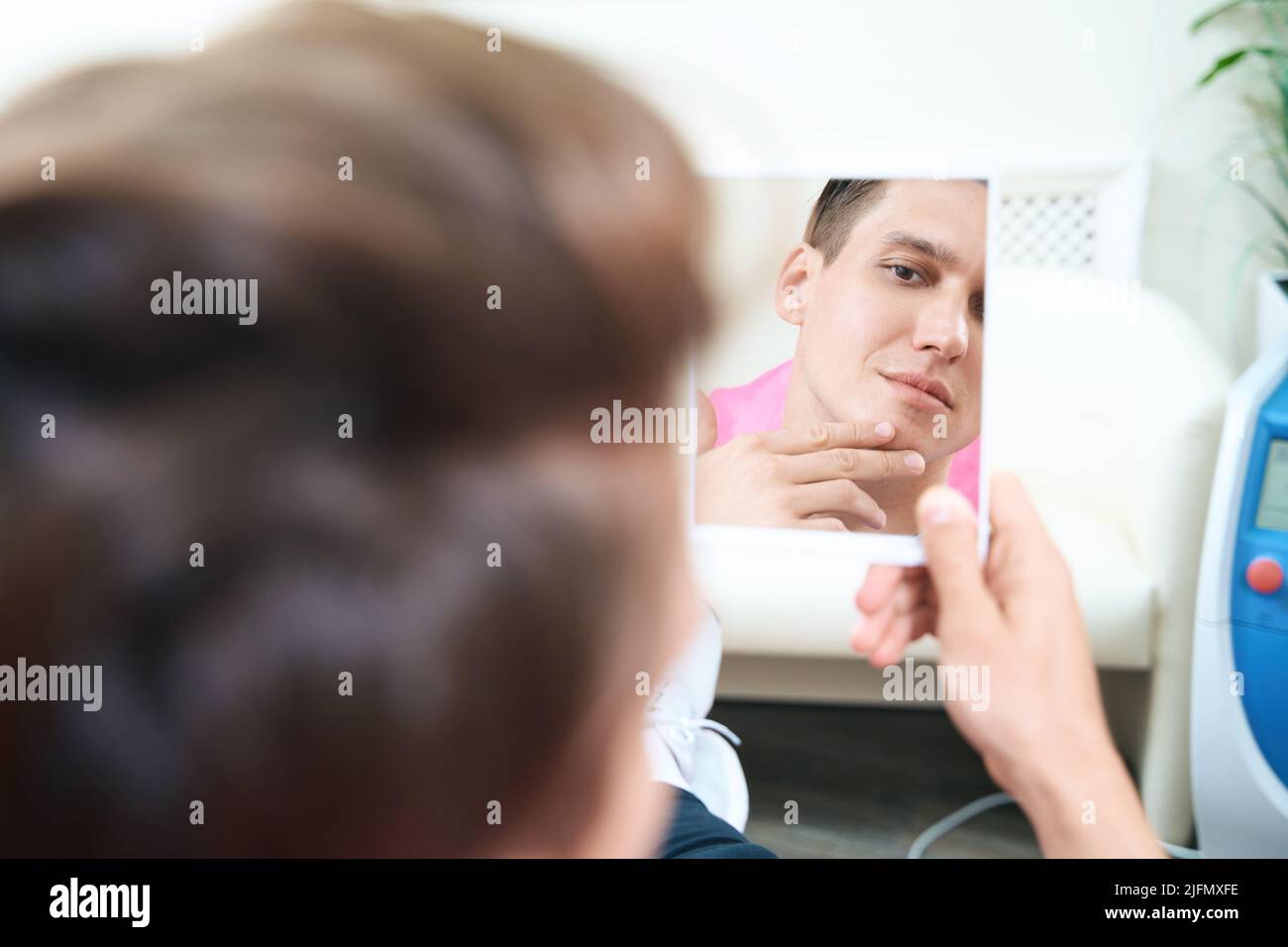 Giovane uomo che stima i risultati dopo le procedure cosmetologiche Foto Stock