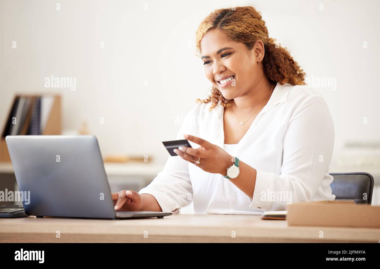Gara mista felice donna d'affari utilizzando una carta di credito e lavorando su un portatile per fare acquisti online al lavoro. Donna ispanica che paga per un acquisto. Femmina Foto Stock