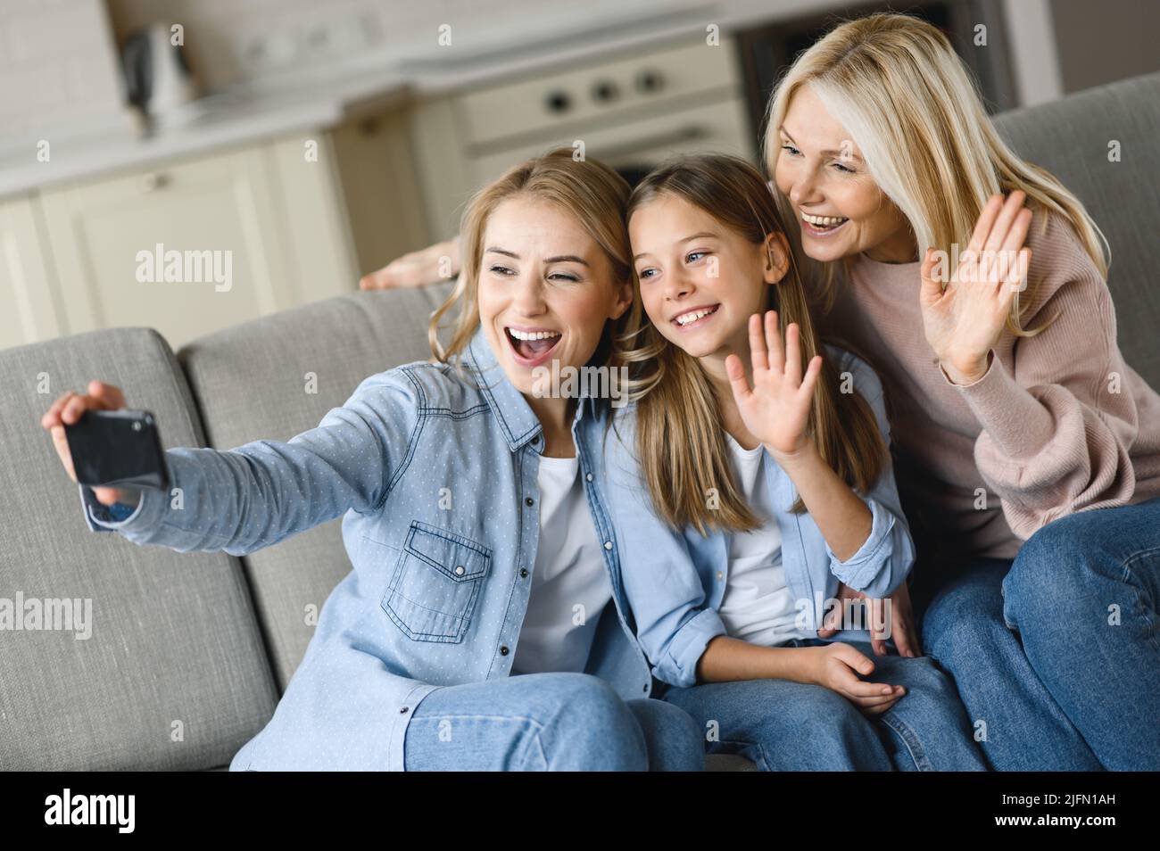 Tre generazioni di femmine caucasiche. Buona nonna, figlia e nipote, seduta sul divano in soggiorno, divertirsi insieme, prendere selfie in posa per la fotocamera, parlare con una videochiamata Foto Stock