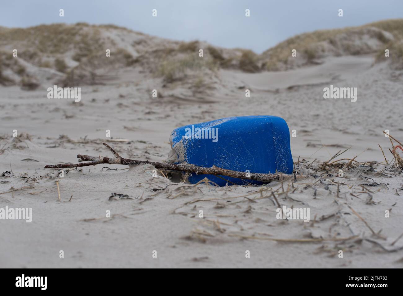 primo piano di un barattolo di plastica blu lavato / jerrycan sulla spiaggia di fronte alle dune di sabbia Foto Stock