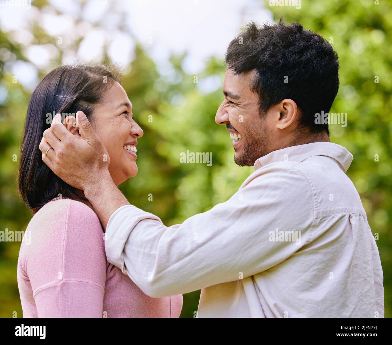 Amorevole marito che mette i capelli dietro l'orecchio dei wifes in piedi faccia a faccia in un parco. Momenti felici e romantici di una bella coppia che trascorrono del tempo insieme all'aria aperta Foto Stock