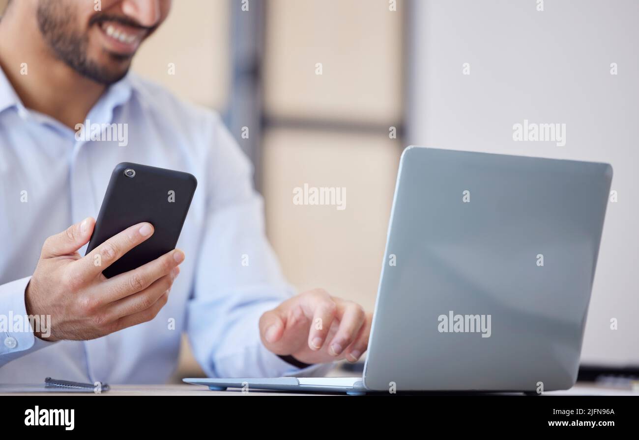 Primo piano di un uomo d'affari che utilizza smartphone e laptop in ufficio. Uomo che utilizza l'app per telefono cellulare per sincronizzare i dati con il computer portatile. Ottenere conferma Foto Stock