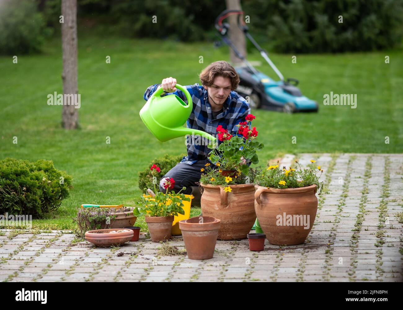 Giovane uomo che innaffia fiori in vaso in giardino in primavera Foto Stock
