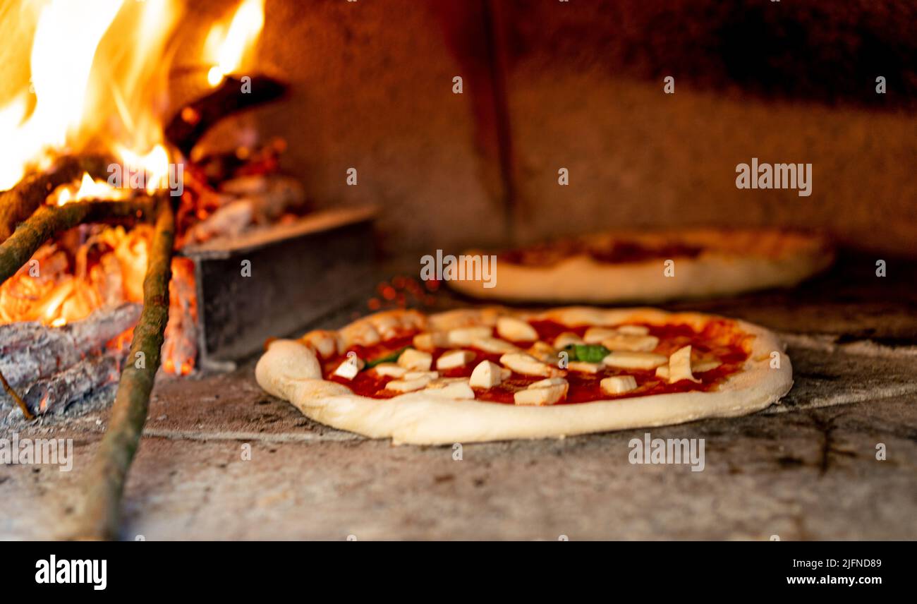 pizza tradizionale napoletana che si inforna forno a legna con spazio copia, sullo sfondo fiamme e legno marchiatura, pizza margherita con basilico Foto Stock