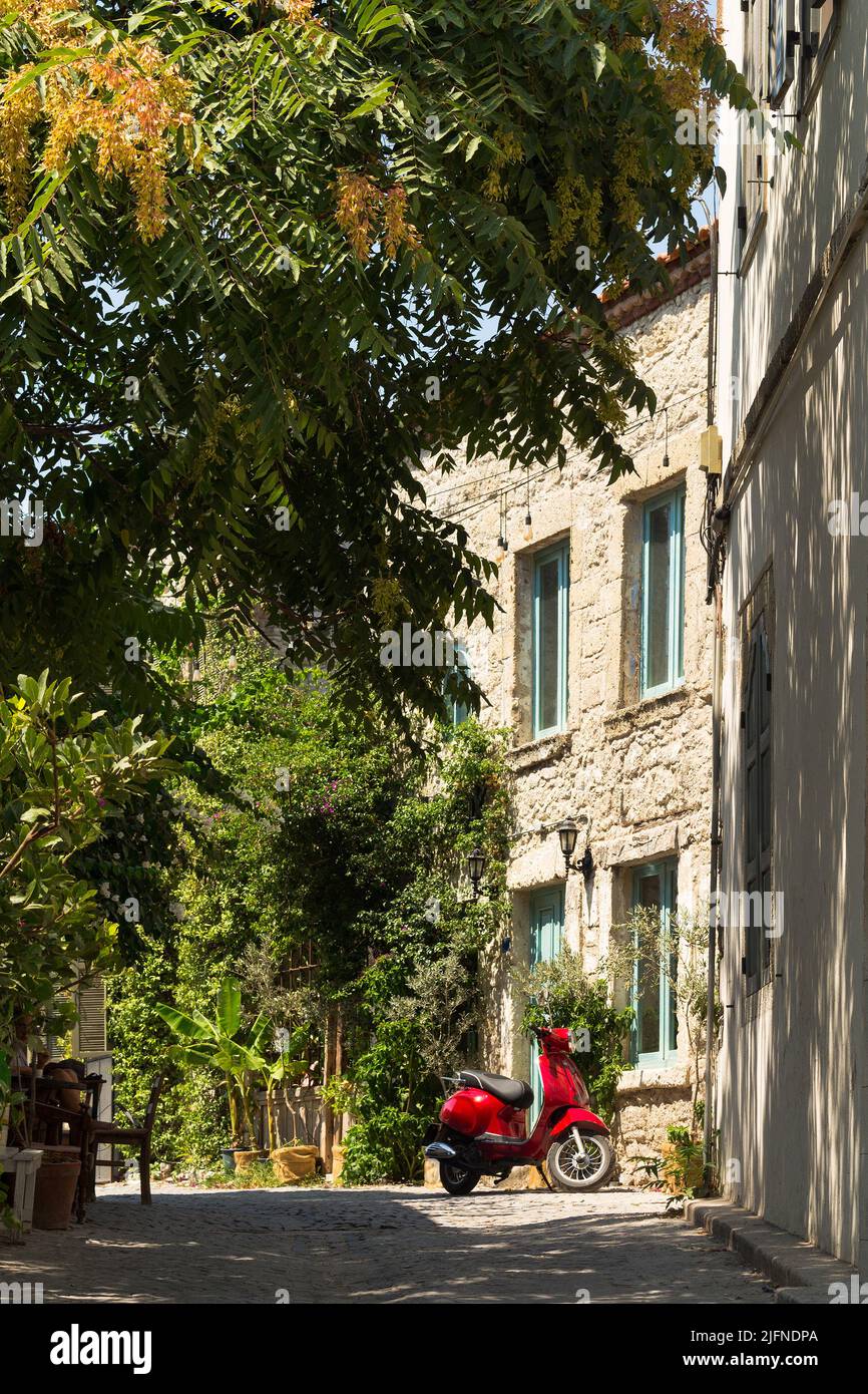 Vista di una moto rossa, alberi e vecchie case storiche in pietra tradizionale nella famosa città turistica del mar Egeo chiamata Alacati. È un villaggio di Cesm Foto Stock