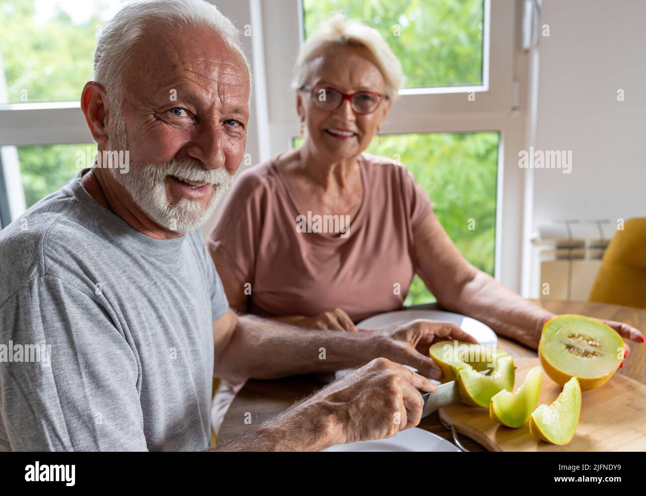 Coppia anziana seduta al tavolo da pranzo a casa e mangiare melone in estate Foto Stock
