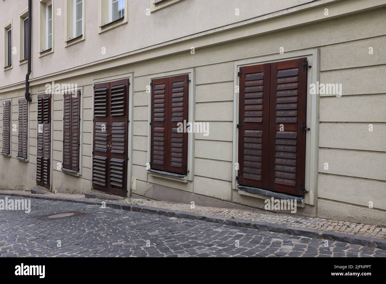 Facciata di edificio con serrande chiuse di legno scuro di fronte a porte e finestre su una strada in Bratislava; concetto chiuso Foto Stock