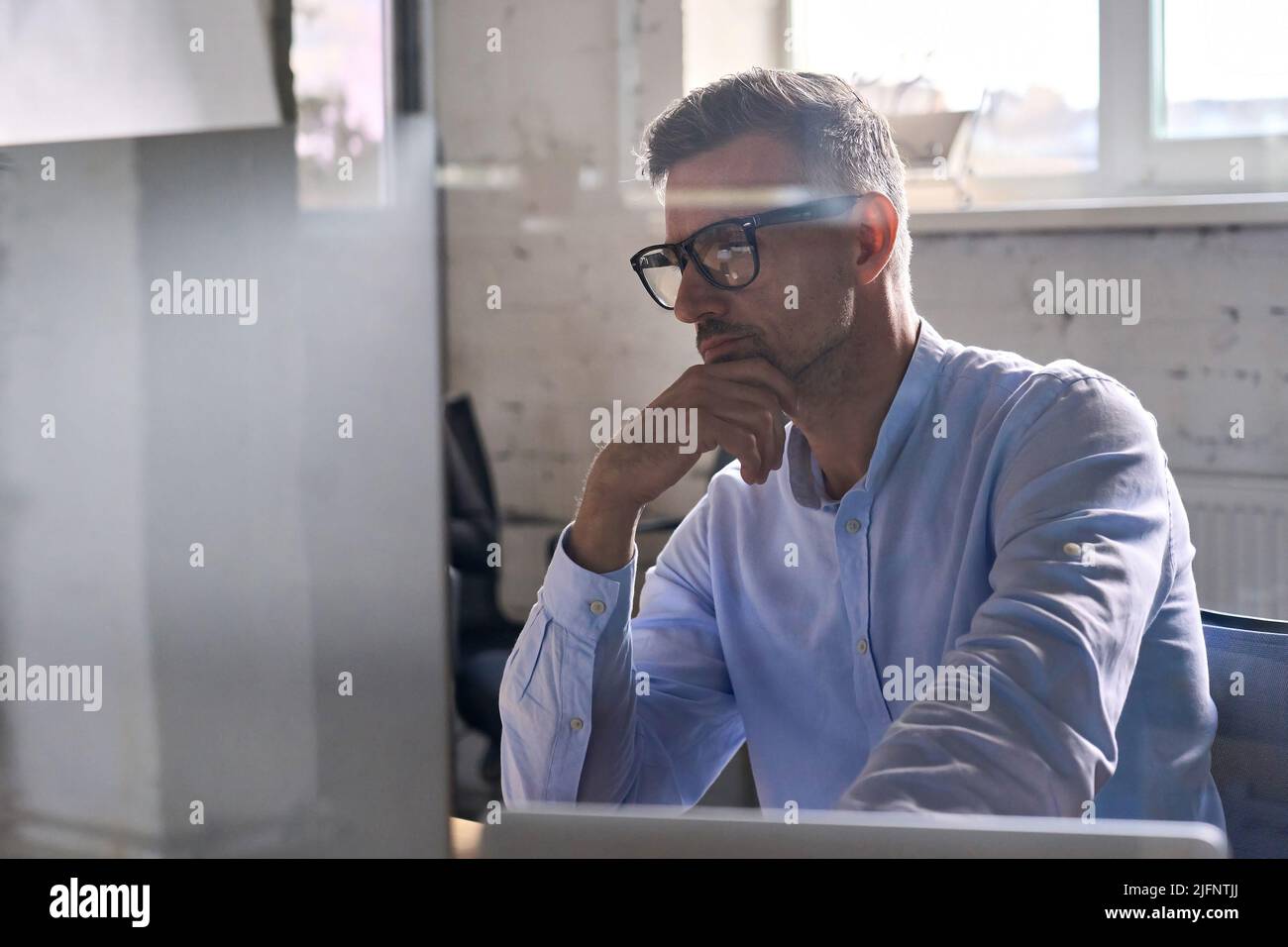 Uomo d'affari attento che lavora usando il calcolatore nell'ufficio moderno al tavolo. Foto Stock