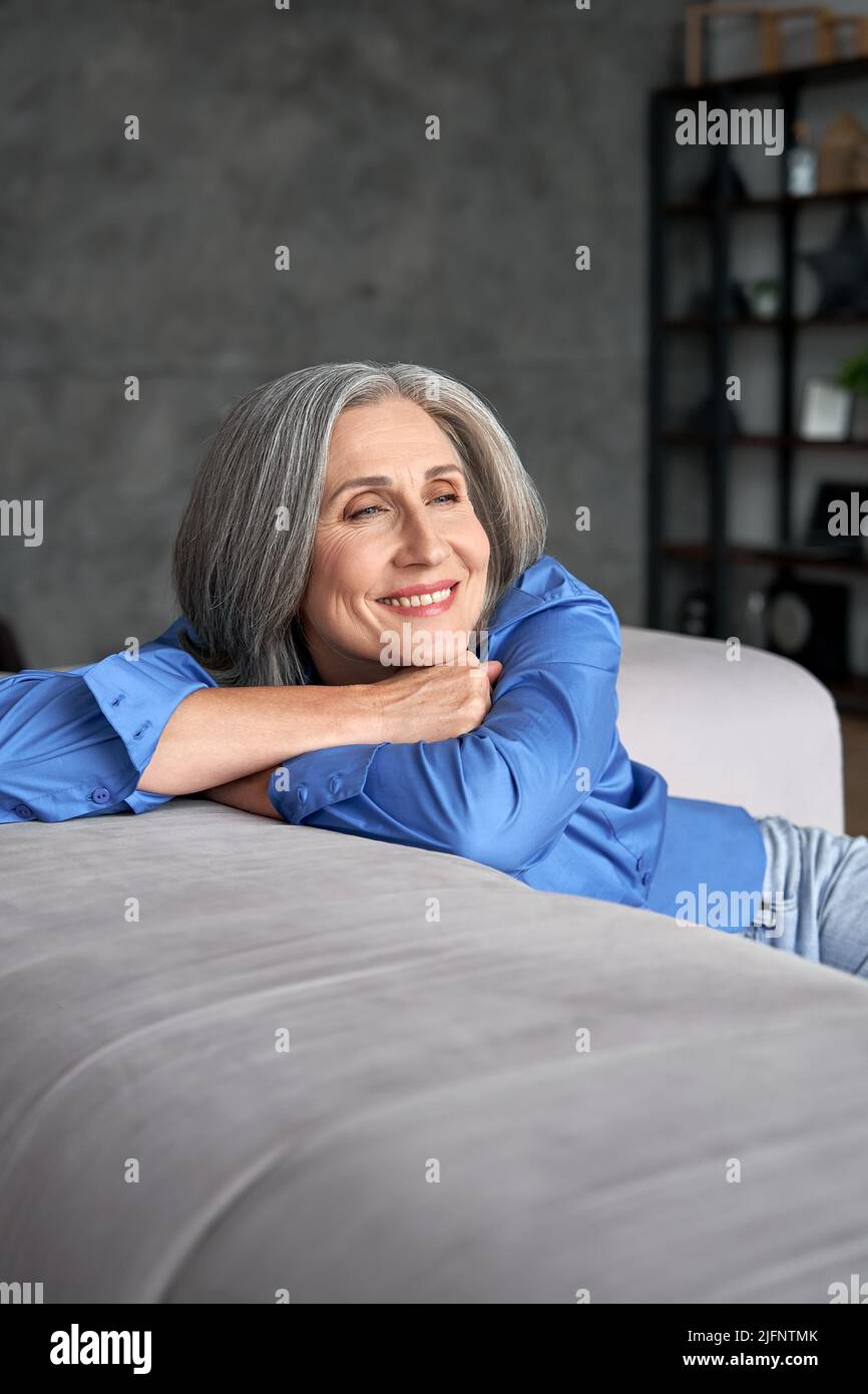 Sorridente vecchia donna matura e riposante sognando seduta sul divano a casa. Foto Stock