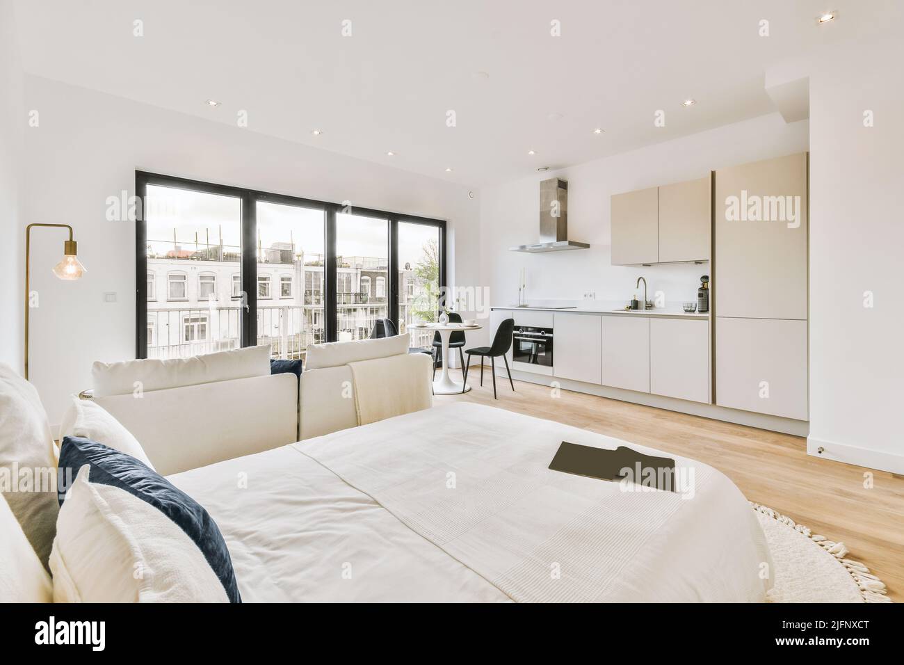 Moderno monolocale dal design minimalista interno con cucina bianca aperta e zona pranzo con tavolo e sedie, zona soggiorno e ampio letto confortevole Foto Stock