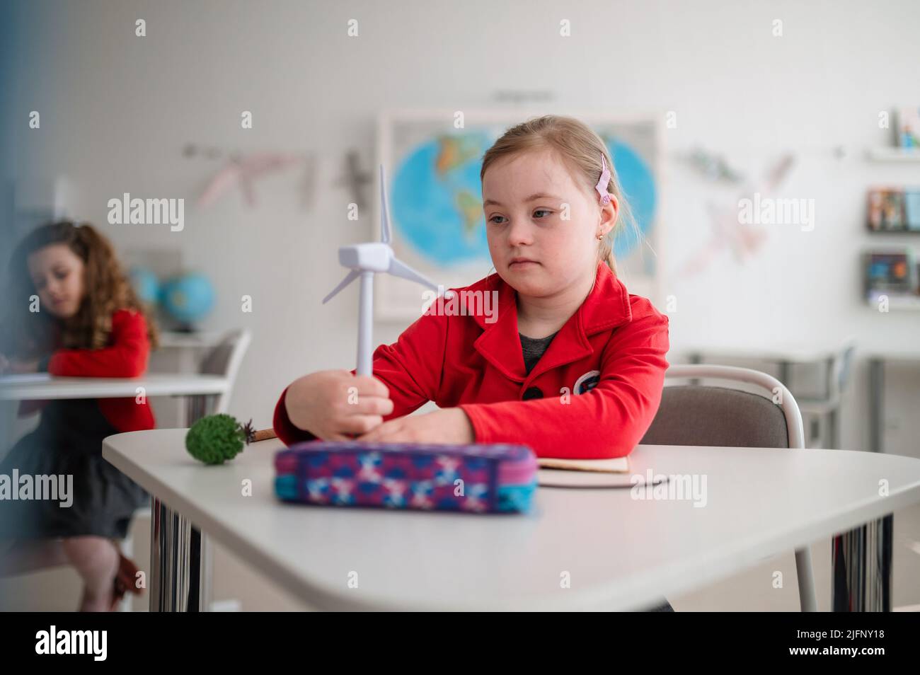 Down sindrome scolgirl con modello di turbina eolica imparare a conoscere le fonti di energia rinnovabili eco-compatibili in classe a scuola, concetto di integrazione. Foto Stock