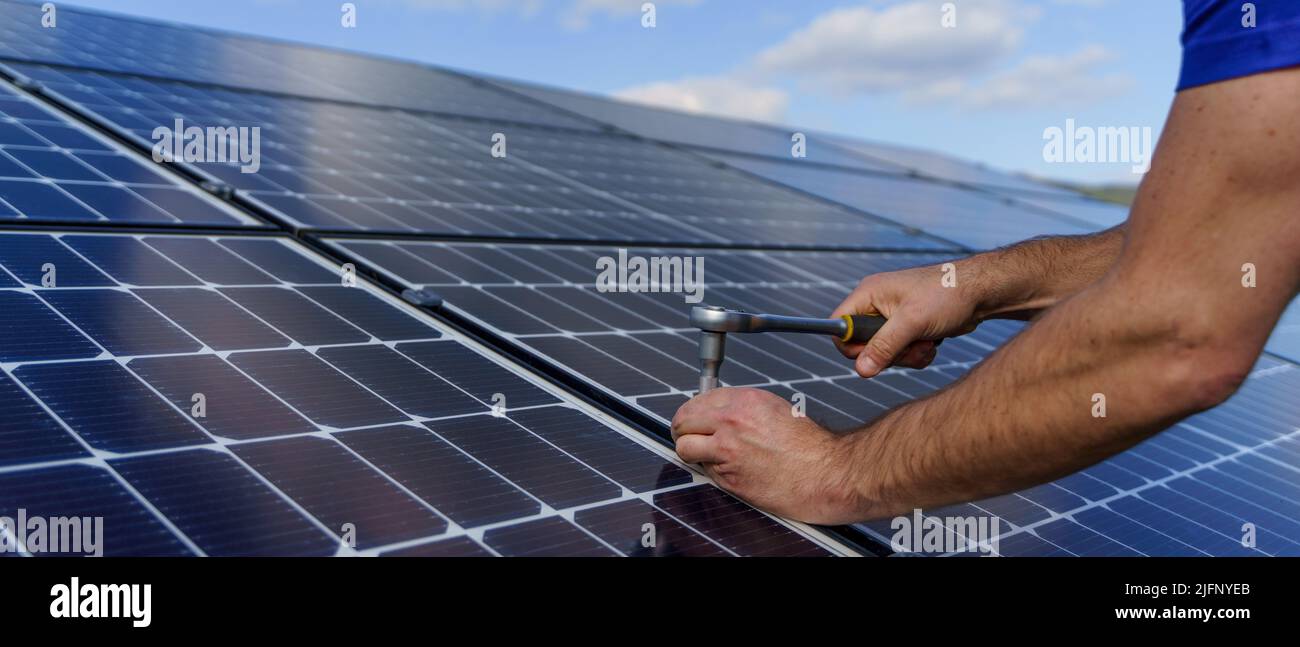 Uomo lavoratore che installa pannelli solari fotovoltaici sul tetto, alternative Energy concept.Close up mani con trapano. Foto Stock