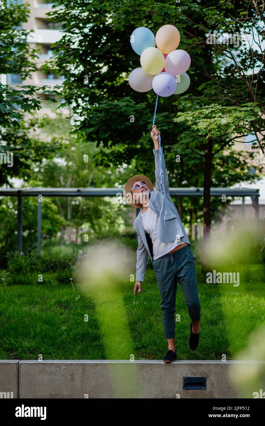 Ritratto divertente di uomo d'affari maturo felice energico tenendo palloncini e camminare sul muro, sentirsi liberi, lavoro vita equilibrio concetto. Foto Stock