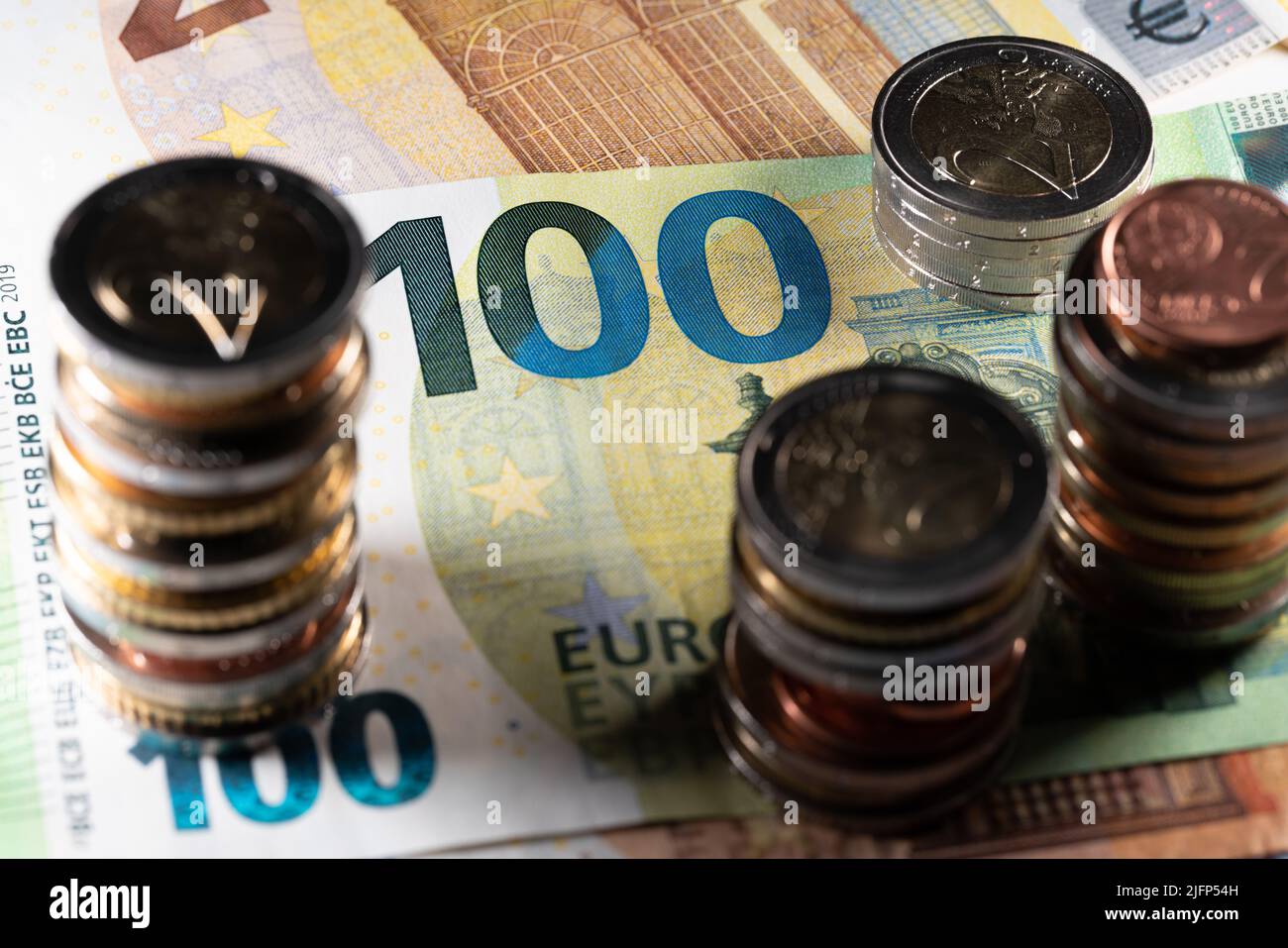 Monete in euro in ombra, monete impilate su cento euro fattura alla luce Foto Stock