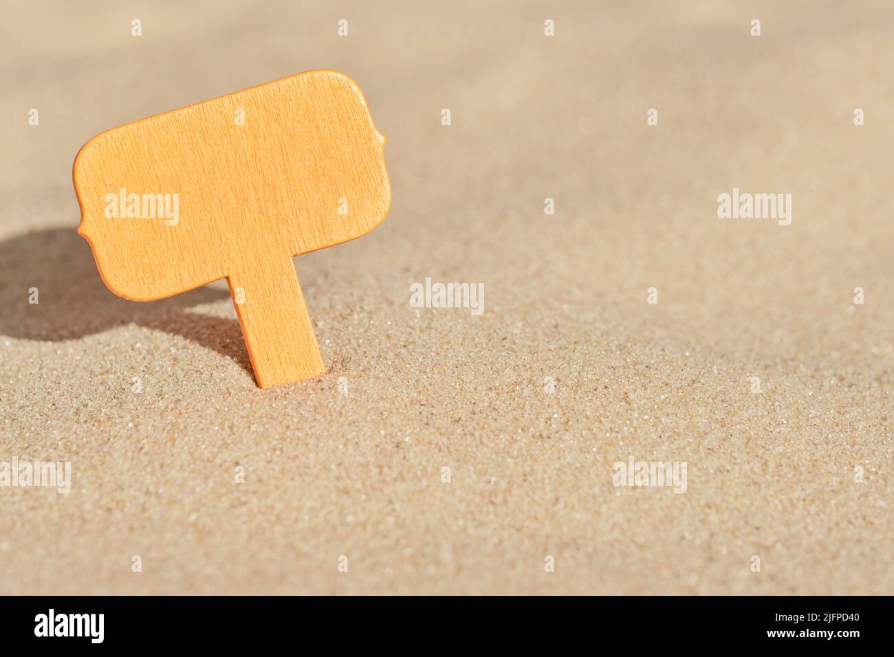 Minimo sfondo estivo, un cartello arancione bianco in legno sepolto nella sabbia della spiaggia una giornata di sole. Design a colori caldi con spazio per la copia. Foto Stock