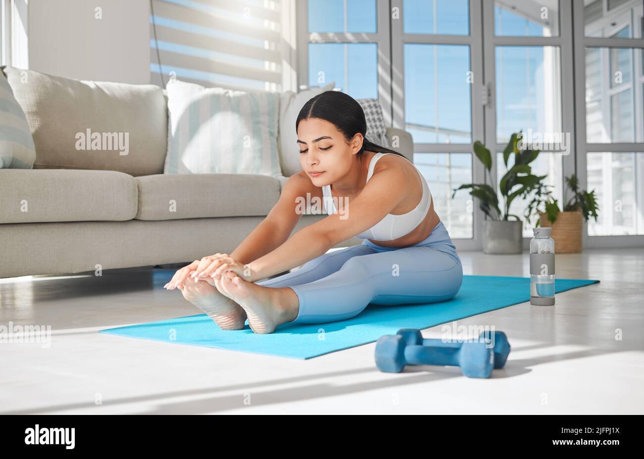 Allungare e aumentare la flessibilità aiuta ad alleviare i muscoli stretti. Scatto di una giovane donna sportiva che si allunga mentre si esercita a casa. Foto Stock