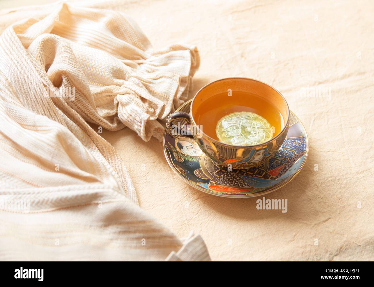 Un primo piano di tazza da tè classica e un pezzo di abiti vecchio stile su un foglio bianco Foto Stock