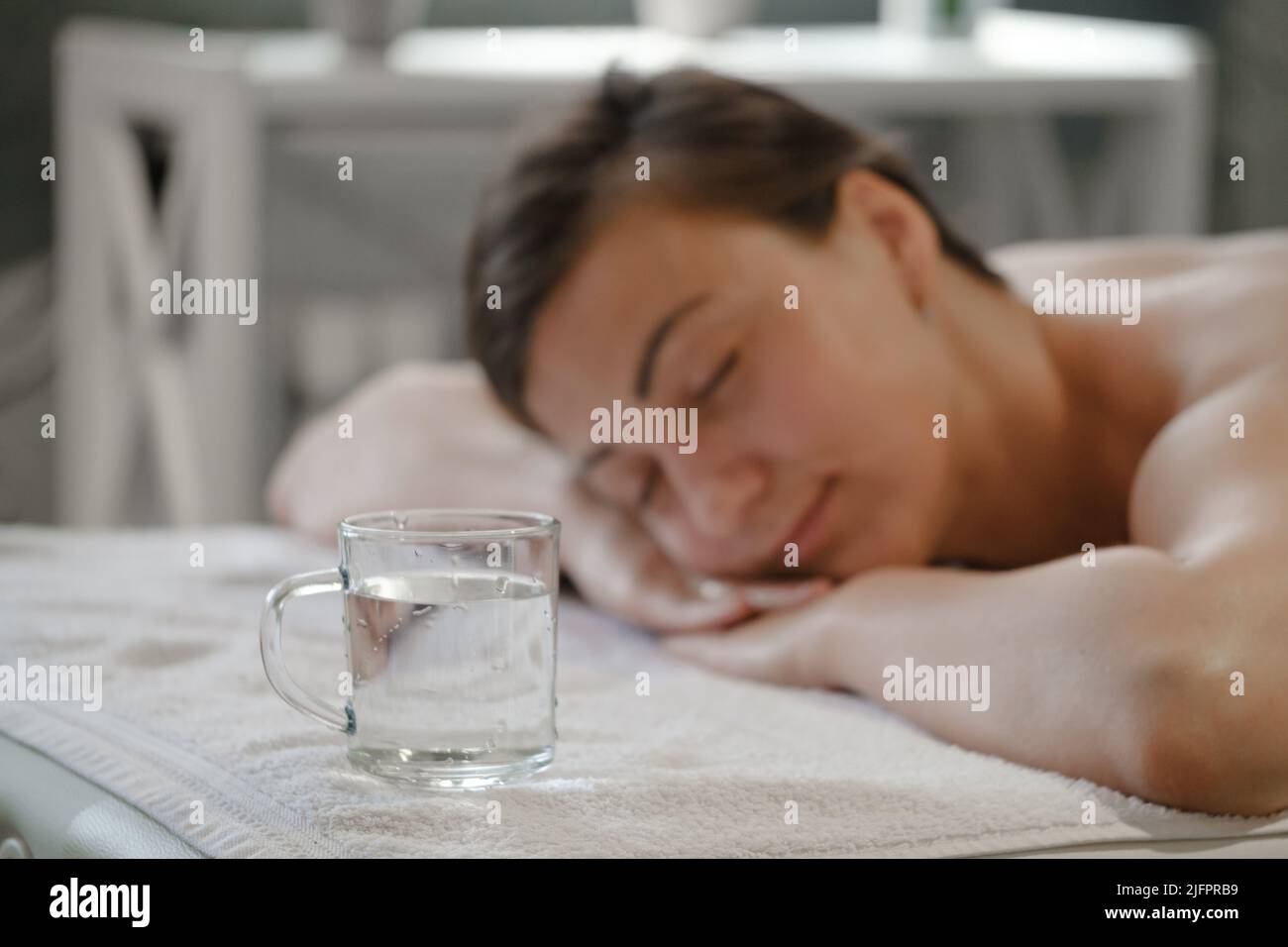 Bella giovane donna con una tazza d'acqua rilassante nel salone termale. Donna in spa in sauna riposo. Rilassamento a vapore caldo. Terapia disintossicante della pelle. Godetevi il caldo Foto Stock