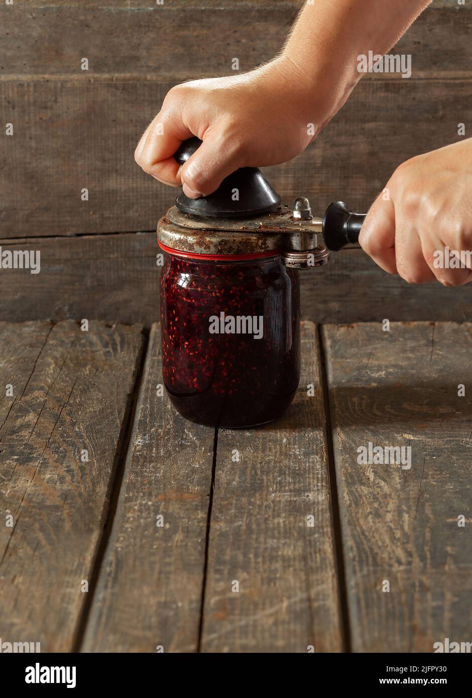 Le mani delle donne arrotolano il coperchio su un vaso di marmellata di lamponi. Conservazione, cottura, cibo Foto Stock